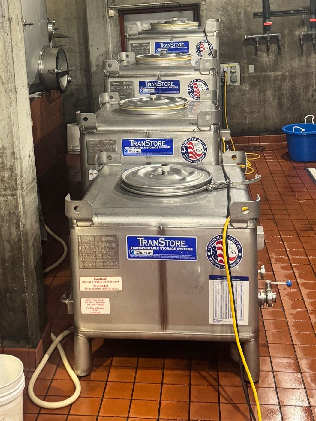 A row of TranStore stainless tanks lined up on a tile cellar floor